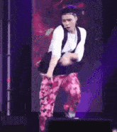 a man in a white shirt and pink pants is dancing on a stage in front of a purple background .