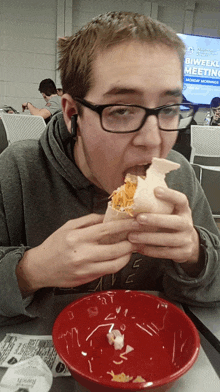 a man eating a sandwich in front of a sign that says biweekly meetings