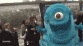 a blue monster with a big eye is standing in a crowd of people