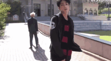 a man in a black jacket with the word army on the sleeve is walking down a sidewalk next to another man .