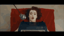 a woman is laying on a red couch with a microphone hanging from her head .
