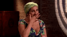 a woman wearing a green turban is covering her mouth with her hand .