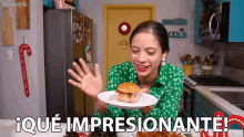 a woman in a green shirt is holding a white plate with a sandwich on it and says iqué impresionante