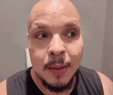 a bald man with a beard is making a funny face while wearing a black tank top .