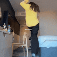 a woman in a yellow sweater is standing on a chair in a room with zoomies written on the bottom right