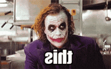 the joker is wearing a purple suit and making a funny face while sitting in a kitchen in a kitchen .