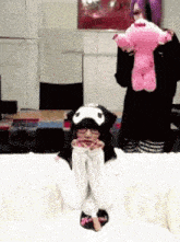 a girl in a cat hat is sitting on a bed holding a pink stuffed animal .