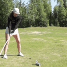 a woman is swinging a golf club at a golf ball on a golf course