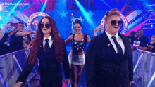 two women in suits and sunglasses are walking through a tunnel with a banner that says chelsea green