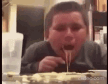 a young boy is eating a slice of pizza with cheese dripping out of it .