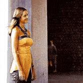 a woman in a yellow top and black pants is standing in a hallway next to a wall .