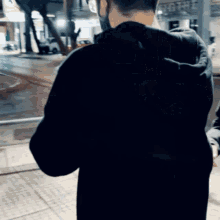 a man wearing a mask and a black hoodie stands in front of a building that says ' a ' on it