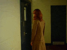 a woman in a brown suit stands in a hallway next to a black door