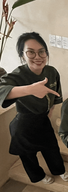 a woman wearing glasses and a khaki shirt points to the right