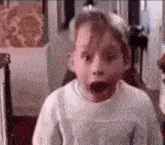 a young boy is making a surprised face with his mouth open in a room .
