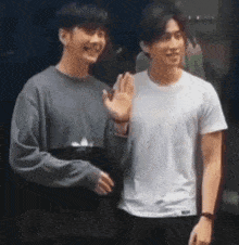 two young men are standing next to each other waving their hands .