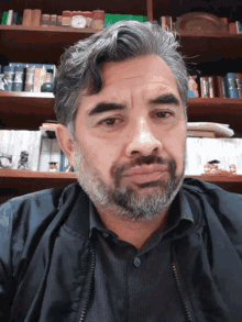 a man with a beard is looking at the camera in front of a bookshelf