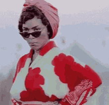 a woman wearing sunglasses and a pink turban is standing in front of a pyramid .