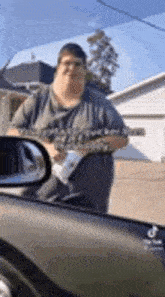 a man is holding a gun while standing next to a car in front of a house .