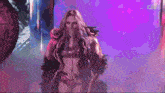 a woman in a feathered outfit is covering her mouth while walking on a stage .