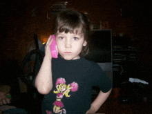 a little girl wearing a black shirt with a mickey mouse on it talking on a pink phone