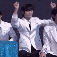 a man in a white suit is sitting next to two other men with their arms in the air
