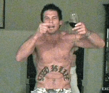 a shirtless man with a tattoo on his stomach is drinking a glass of wine .
