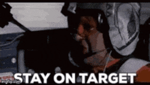 a man in a helmet is sitting in a car with the words `` stay on target '' written on the screen .