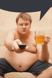 a shirtless man sits on a couch holding a remote control and a glass of beer