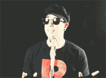 a man wearing sunglasses and a hat is singing into a microphone with the letter r on his shirt