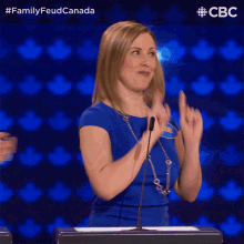 a woman in a blue dress applauds in front of a microphone with the hashtag familyfeud canada