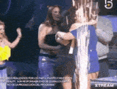 a woman is hugging another woman who is wearing a shirt that says ' xstream ' on it