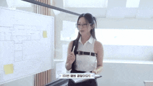 a woman in a white shirt and black pants is standing in front of a whiteboard .