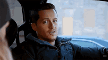 a man in a black jacket is sitting in the back seat of a car and looking out the window .