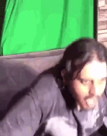 a man is sitting on a couch with a green screen in the background .