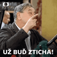 a man in a suit is pointing at his nose with the words uz bud zticha behind him