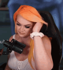 a woman with orange hair is sitting in front of a microphone and covering her ears .