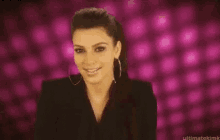 a close up of a woman wearing hoop earrings and a black jacket on a pink background .