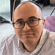 a bald man wearing glasses and a plaid shirt looks at the camera .