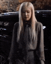 a woman with long blonde hair is standing in front of a black car .