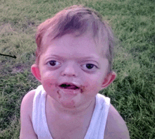a little boy with a dirty face is sitting in the grass