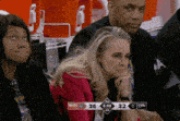 a woman sits in the stands watching a basketball game with the scoreboard showing 36 to 32