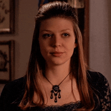 a woman wearing a black lace top and a necklace with a pendant on it