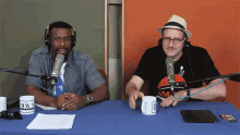 two men sit at a table with microphones and a mug that says raw a on it