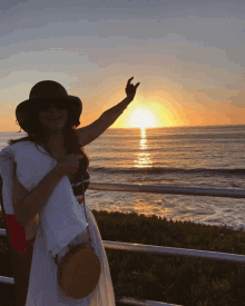 a woman wearing a hat stands in front of the ocean at sunset