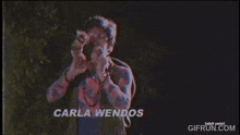 a man in a plaid shirt is holding a camera in front of his face and says carla wendos .