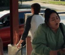 a woman in a green shirt stands in front of a gas pump that says rp