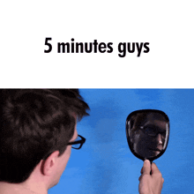 a man looking at his reflection in a hand mirror with the words " 5 minutes guys " below him