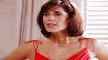 a woman in a red dress is standing in front of a window with blinds