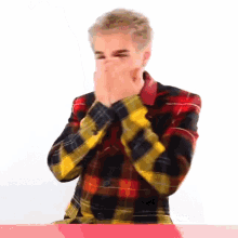 a man in a plaid shirt covering his face with his hands